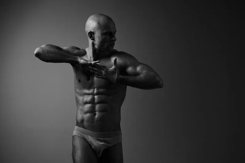 Athletic man flexing his muscles in a powerful pose, showcasing strength and determination in black and white tones. This striking image captivates attention with its intensity.