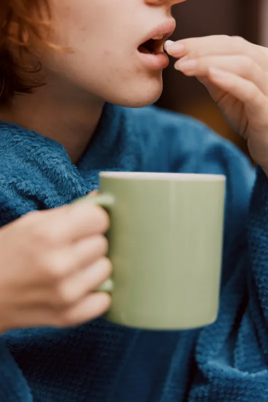 Женщина в синем халате держит чашку кофе и смотрит в камеру с открытым ртом