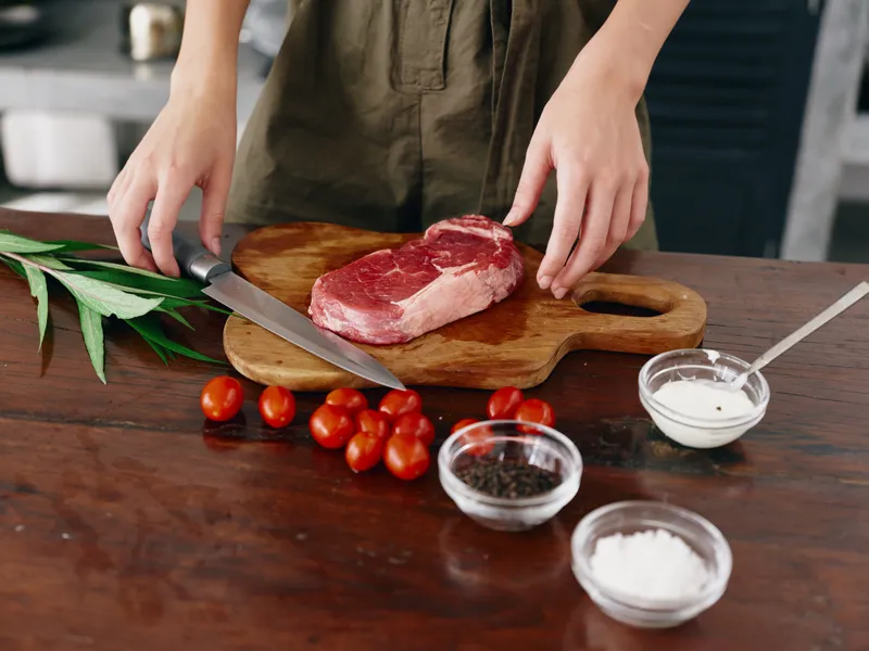 Женщина с ножом в руке нарезает мясо стейка для жарки на кухне