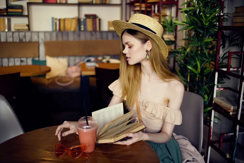 Весёлая женщина читает книгу в кафе, стильно одета