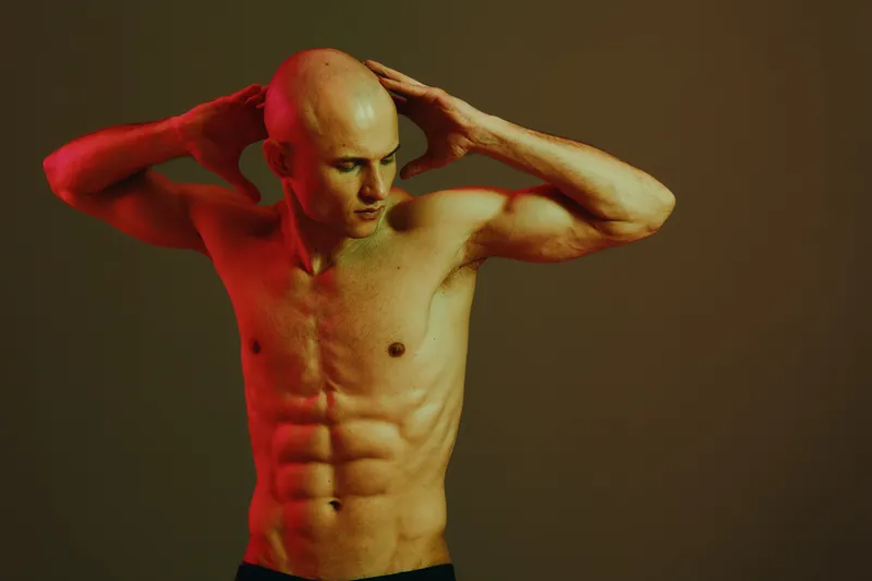 Muscular man posing with expressive gestures, showcasing a strong physique. This vibrant image captures confidence and determination against a dark background.