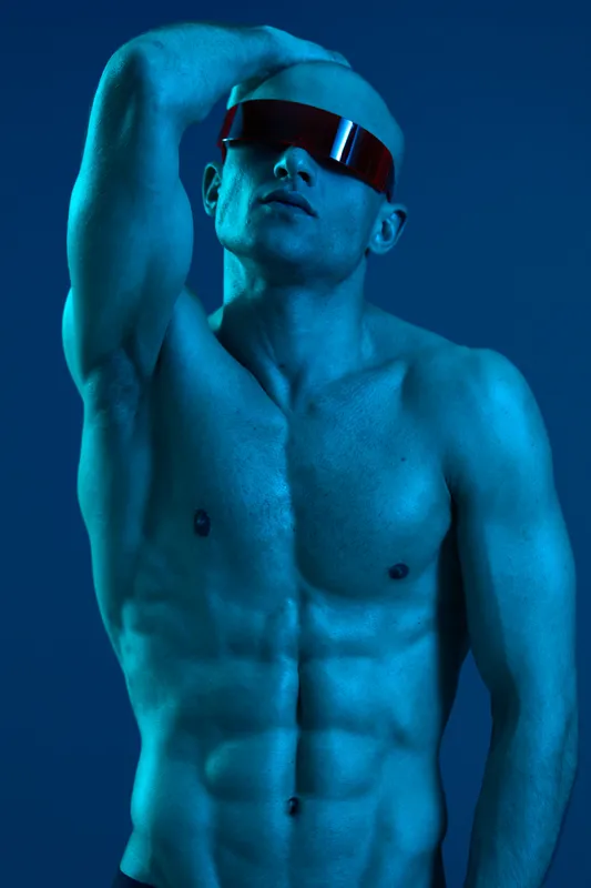 A striking image of a man with a toned physique, wearing futuristic sunglasses against a blue background. The scene conveys confidence and modern style in a vibrant atmosphere.