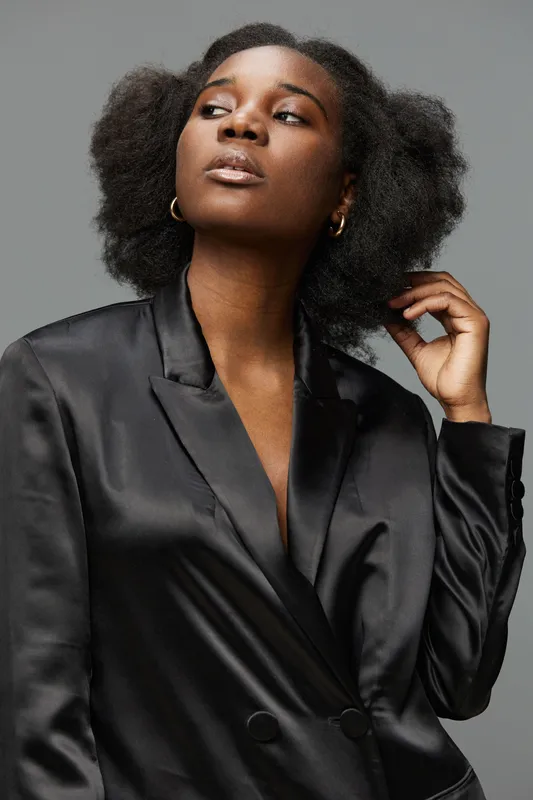 Elegant Black Woman in Satin Blazer, Exuding Confidence and Style Against a Neutral Background