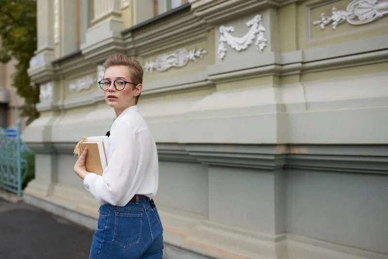 Студент в очках прогуливается по городу с книгой, общаясь