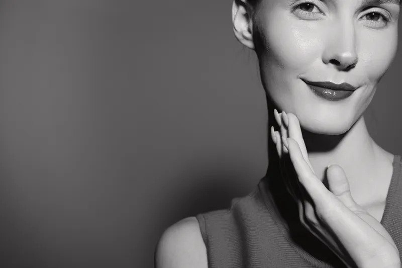 Close-up of a smiling caucasian woman with fair skin touching her face, black and white studio portrait. Concept of beauty skincare and facial care.