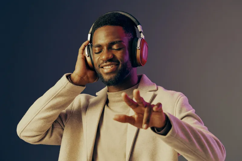 Young Black man enjoying music with headphones on a colorful background, expressing joy and relaxation through his emotions