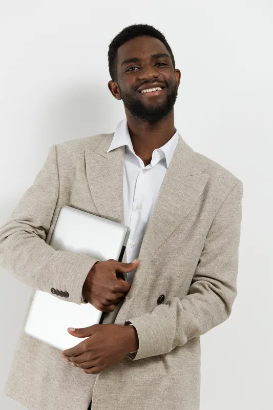 Confident smiling man in beige blazer and white shirt holding a closed tablet computer isolated on plain white background. Business casual style, professional look, young adult, foreground portrait, s
