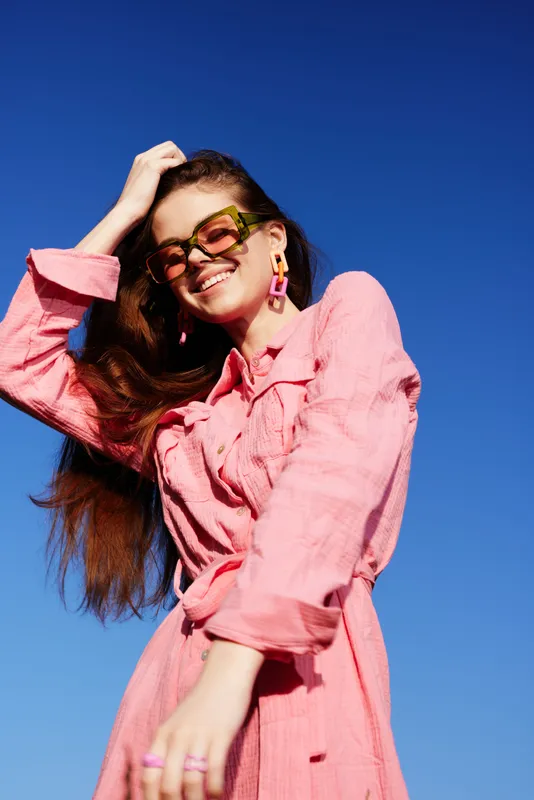 Young woman in a pink summer dress enjoying the sun, showcasing vibrant emotions against a clear blue sky during a sunny day outdoors