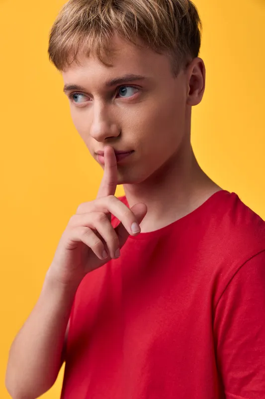 Shh gesture by a youth in a red shirt against a warm yellow backdrop, capturing secrecy, quiet moment, contemplation, and a thoughtful mood in a minimalist studio scene