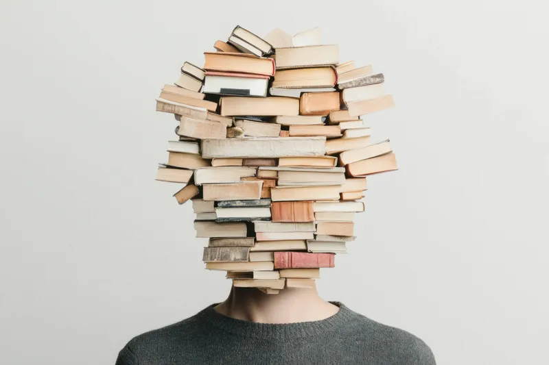 Это уникальное концептуальное изображение показывает человека, голова которого состоит из стопки книг, что олицетворяет образование и стремление к знаниям