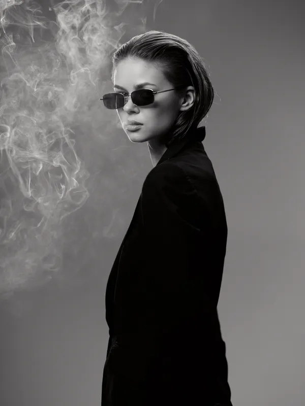 Black and white portrait of stylish woman in sunglasses with headscarf and smoke background