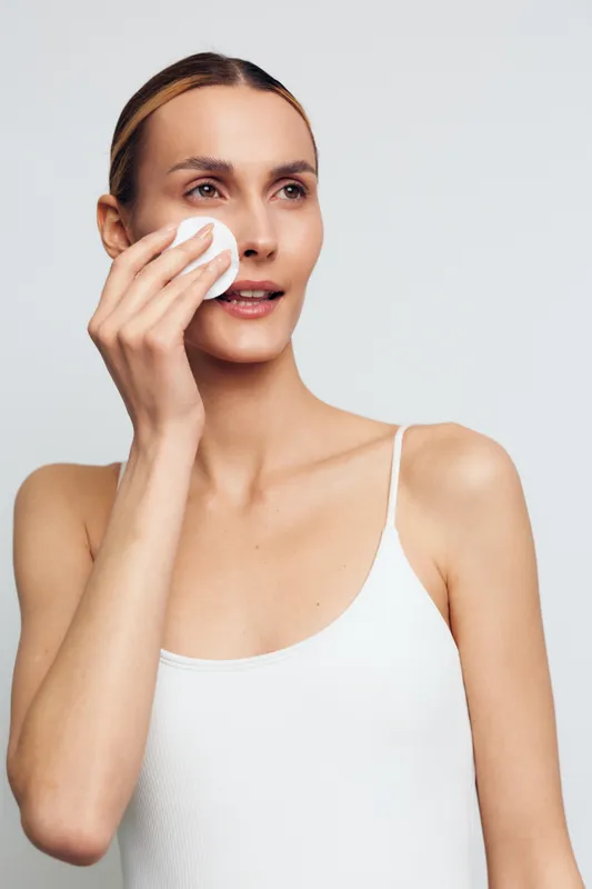 Woman skincare beauty closeup, wiping face with white tissue, hygiene and selfcare on clean studio background, soft light for fresh skin, wellness mood, minimal setting