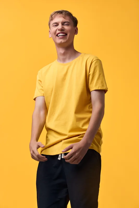 Man wearing a bright yellow t shirt in a studio setting, smiling and relaxed, showcasing casual style and upbeat mood for fashion and lifestyle campaigns