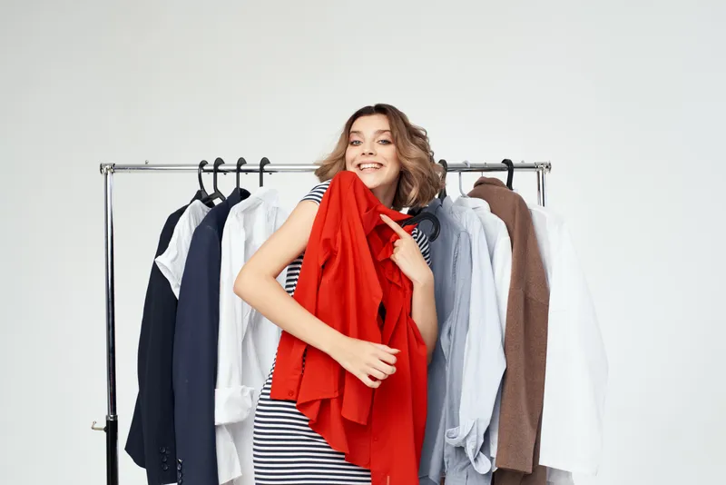Эмоциональная женщина выбирает одежду возле гардероба на светлом фоне