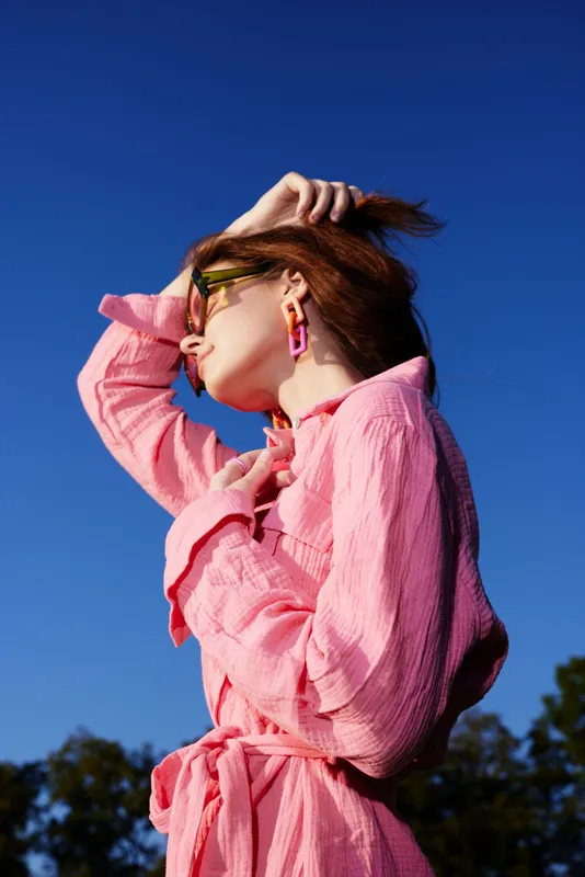 Young woman in a pink dress enjoying the sun against a blue sky, showcasing joy and confidence, perfect for fashion and lifestyle themes