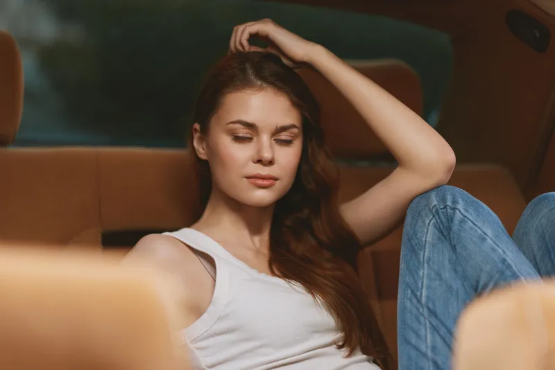 Calm young woman relaxing in a car interior, wearing casual outfit, with a serene expression and soft natural light illuminating her features.