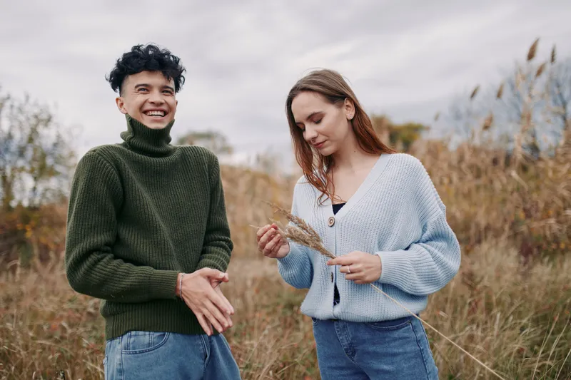 Authentic moment between friends outdoors in a field, candid smiles, natural posture, and genuine mood; simple style conveys a believable, warm connection.