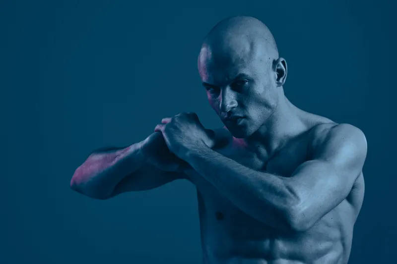 A powerful man poses dramatically with a determined expression, showcasing his physique in a captivating light. Black and white tones enhance the image's intensity.