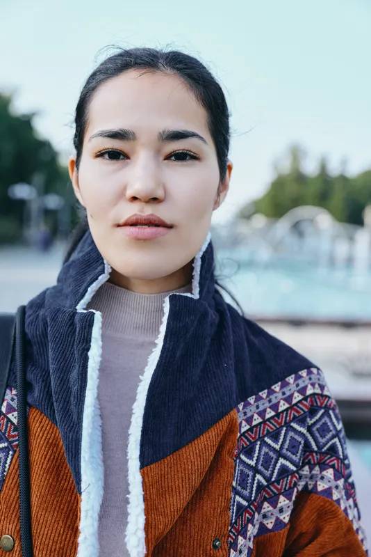 Woman, outdoor pool setting, wearing a patterned jacket and soft sweater, with a calm expression, natural light, casual chic style, summer vibe, fashion forward look, close up scene