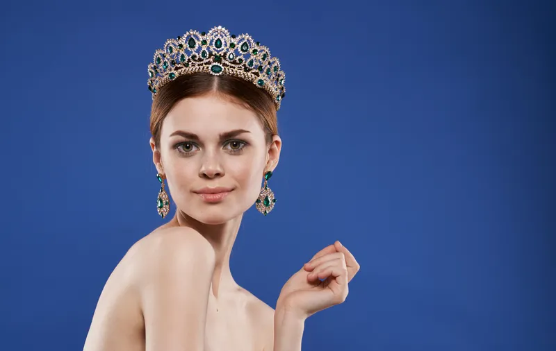 Симпатичная женщина с обнаженными плечами, короной на голове и украшениями на голубом фоне