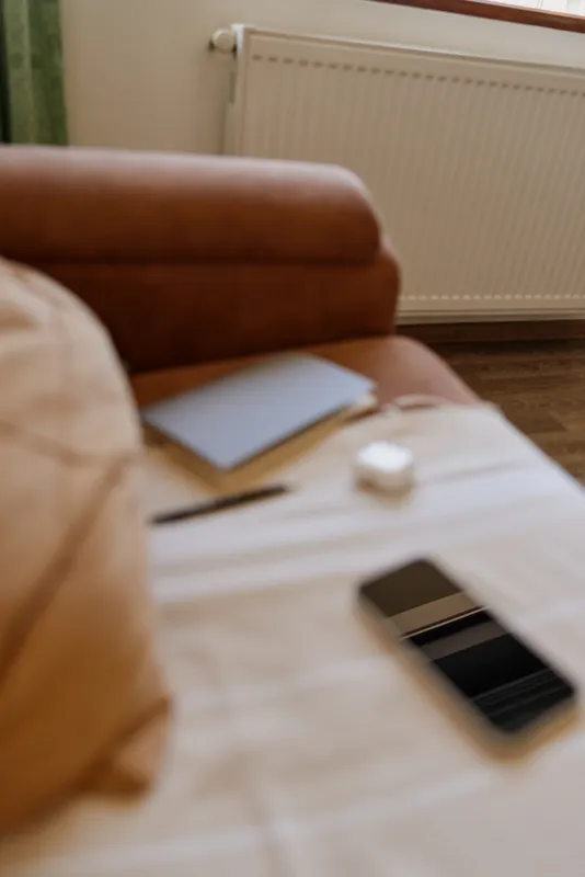 A cozy home living room with a soft brown sofa, notebook and smartphone on a light wooden coffee table. Natural light and a blurred background convey relaxed daily life at home.