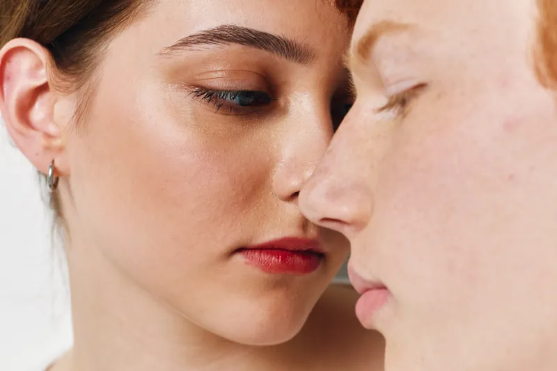Portrait of two young women close together with natural skin, freckles, and minimal makeup for beauty, friendship, and skin care concept in studio lighting.