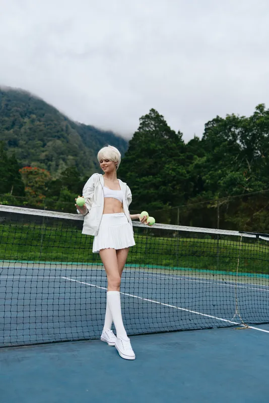 Young female tennis player in stylish sporty outfit, showcasing confidence and focus on court surrounded by lush greenery and mountains