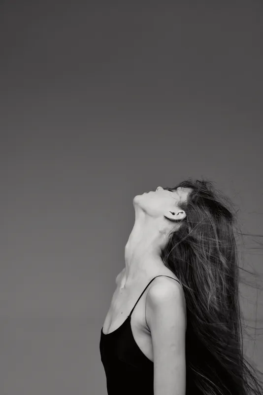 Black and white portrait of a young woman with long hair looking upwards in a minimalist setting