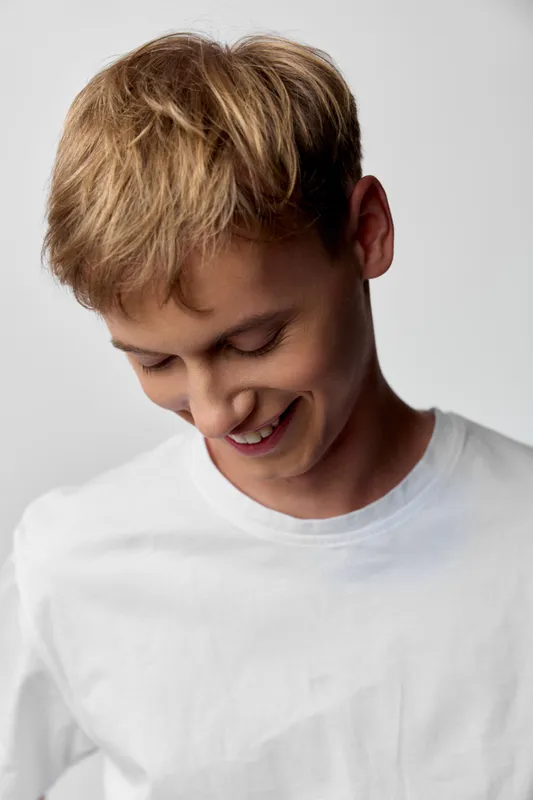 Smiling young man in a white t shirt looking down, casual studio shot conveying warmth, simplicity and natural charm