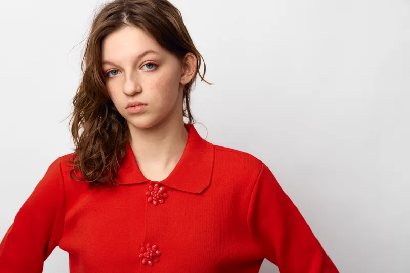 Young woman with wet hair wearing a red sweater looks serious and confident against a white background. Portrait of casual style and natural beauty with minimal makeup.