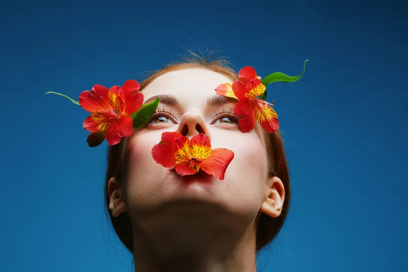 A young woman with vibrant flowers around her face, depicting beauty and nature, with a clear blue background, highlighting emotions of joy and serenity in spring