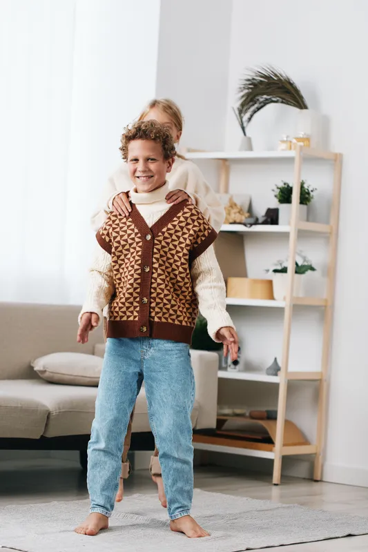 Authentic moment of a child at home, wearing cozy knitwear and denim, smiling with carefree energy, capturing a playful school inspired lifestyle during everyday moments.