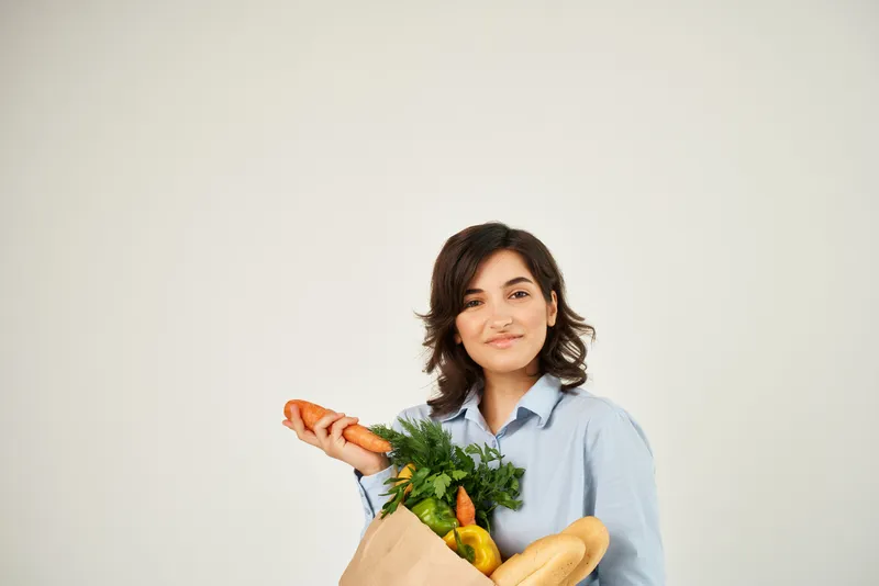 Жизнерадостная женщина с пакетом продуктов, в котором находятся овощи, предназначенным для доставки из супермаркета