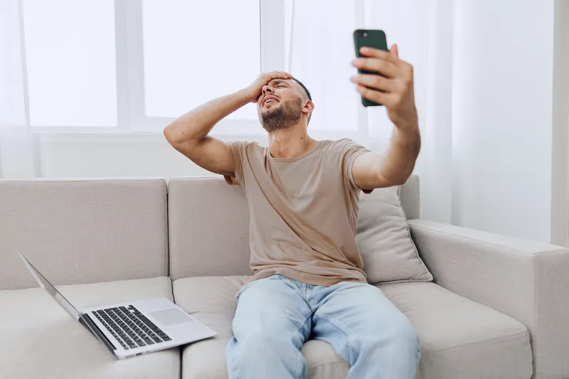 Frustrated man struggling with technology while video calling, showcasing the challenges of remote work. His emotional expression tells the story of modern life.