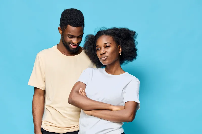 A joyful couple posing against a vibrant blue background, showcasing their stylish casual outfits while expressing happiness and intimacy