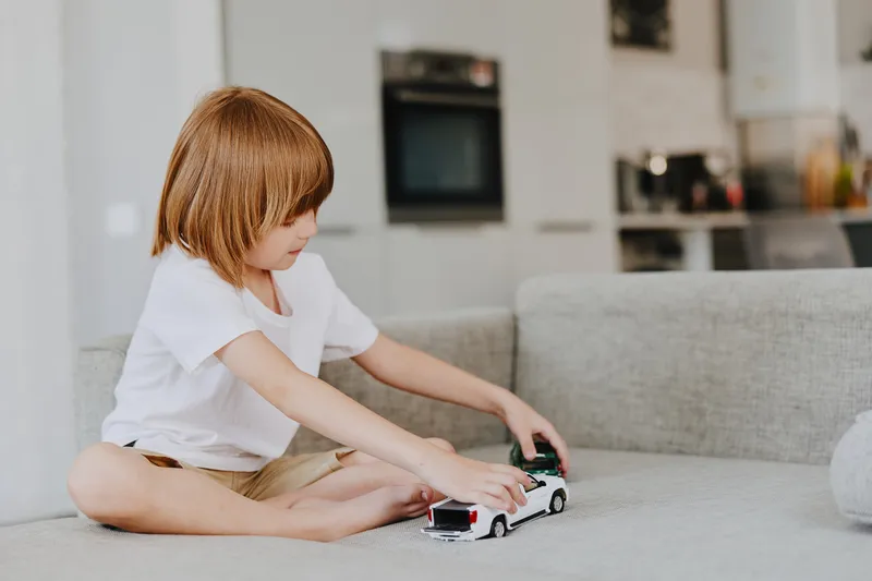 Cute boy playing with toy cars in a cozy living room, showcasing joy and creativity. Perfect for family-oriented themes and childhood happiness.