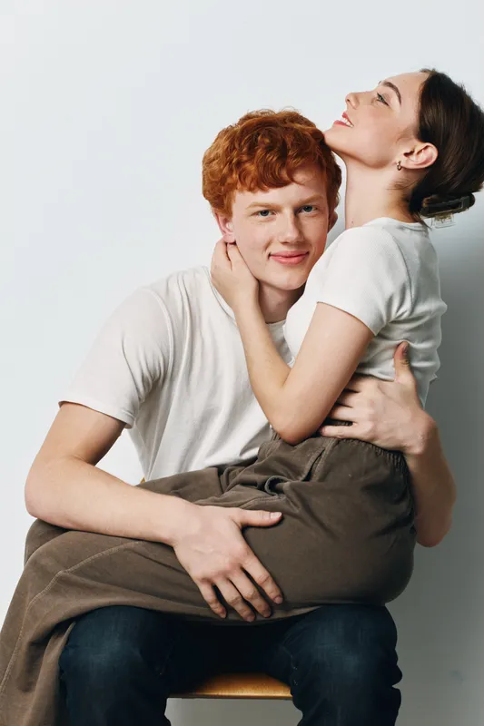 Young couple sitting closely together in casual clothes with affectionate embrace and happy expressions on white background for love and relationship concept.