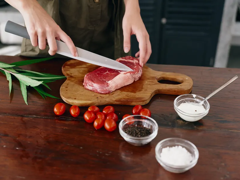 Женщина с ножом в руке нарезает свежее мясо стейка для жарки на кухне