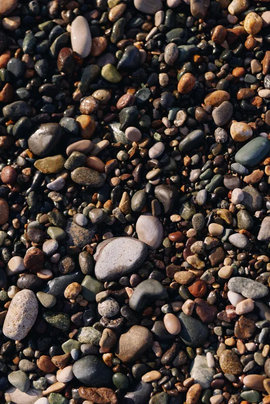 Close up of colorful pebbles and stones scattered on a beach surface, revealing varied shapes and textures for a natural background and tactile detail.