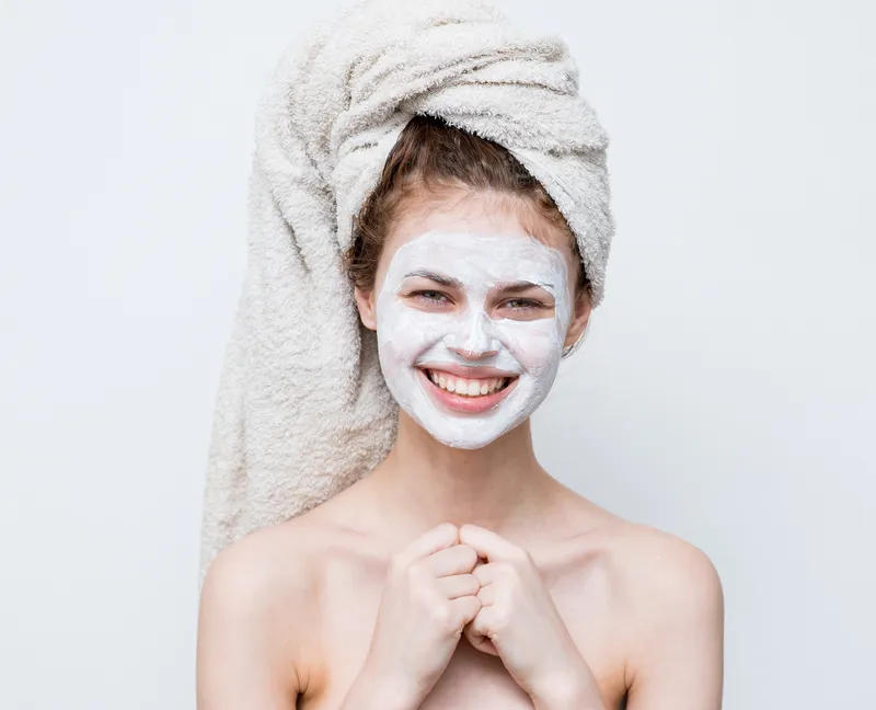 Женщина с обнаженными плечами жестикулирует руками, на лице крем-маска