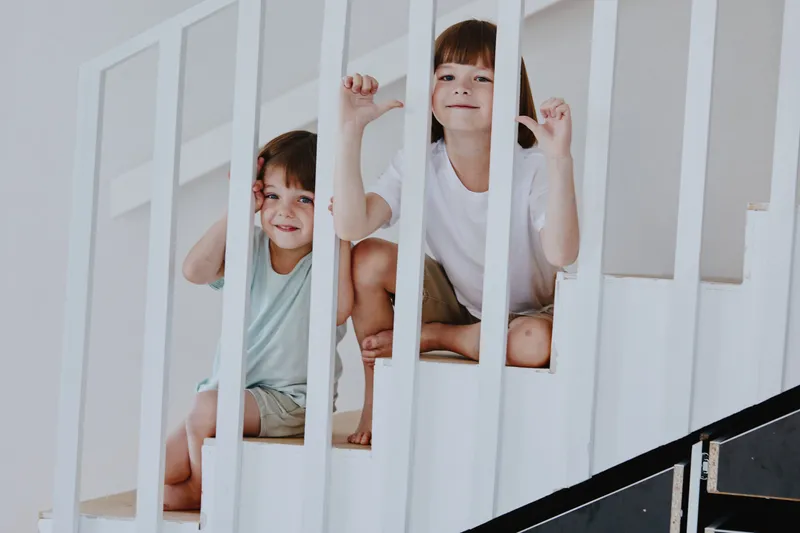 Two playful children enjoying their time on the stairs, showcasing their joyful expressions and carefree spirit in a bright indoor setting.