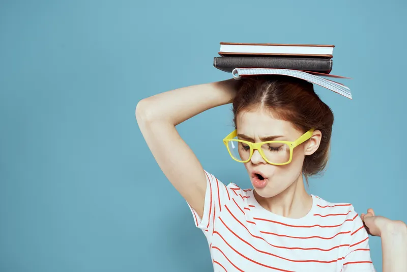 Студентка с книгами на голове и в жёлтых очках на синем фоне, обрезанный вид