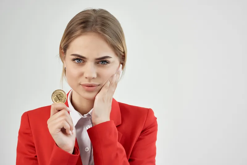 Деловая женщина в красной куртке с золотой монетой Bitcoin на светлом фоне
