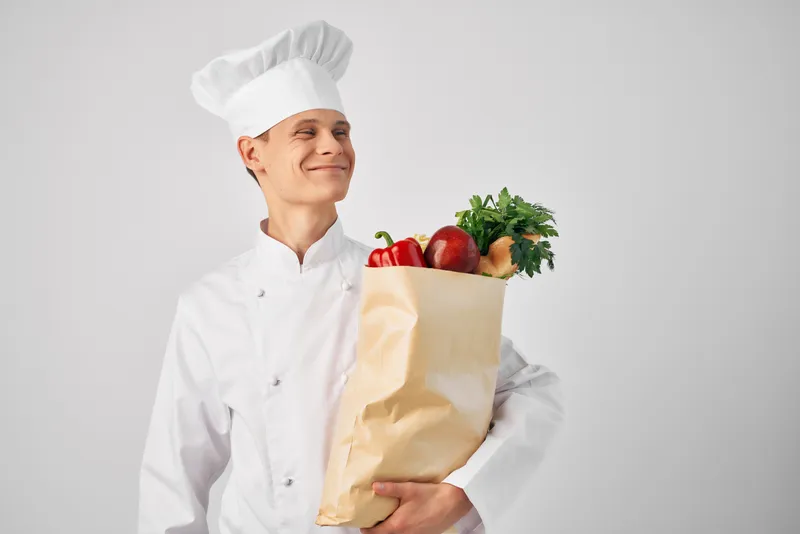 Шеф-повар с пакетом продуктов на кухне занимается приготовлением еды и работой