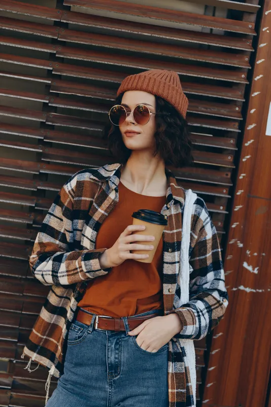woman coffee street fashion sunglasses beanie plaid jeans capture a candid lifestyle portrait of relaxed urban style with authenticity, mindful living, golden hour glow and emotional storytelling.