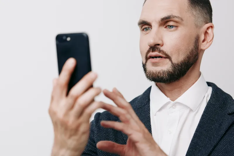 A professional man in a suit uses a smartphone, displaying focused emotion and confidence on an isolated color background, capturing modern business presence.