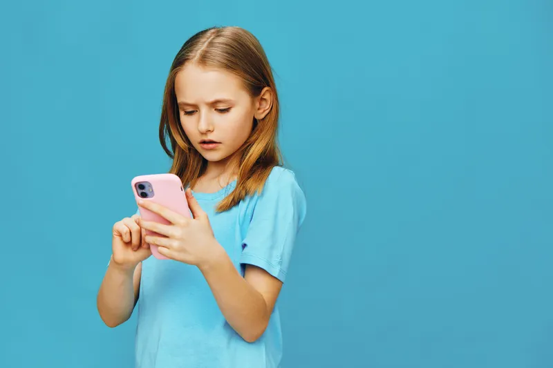 Young girl using smartphone, looking serious, blue background, casual wear, modern technology, focused expression, childhood, digital communication
