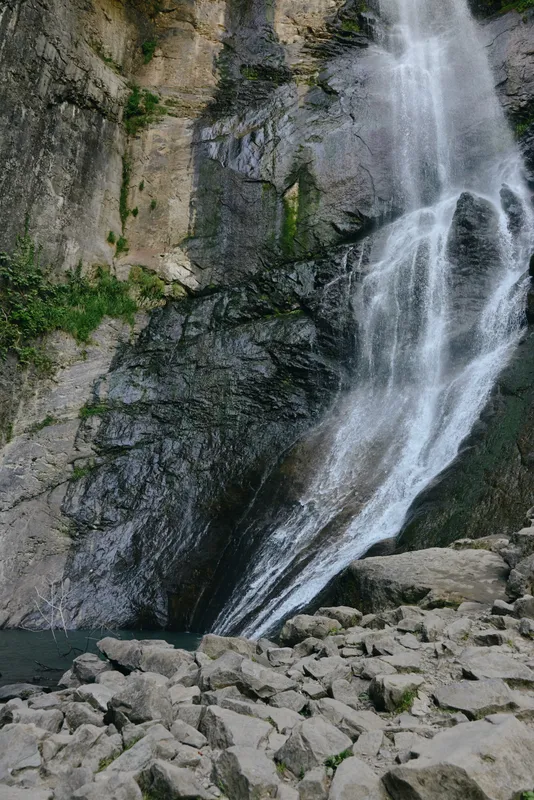 waterfall cascading over rocky cliff with lush green moss and clear water at base surrounded by natural stone landscape in forest setting