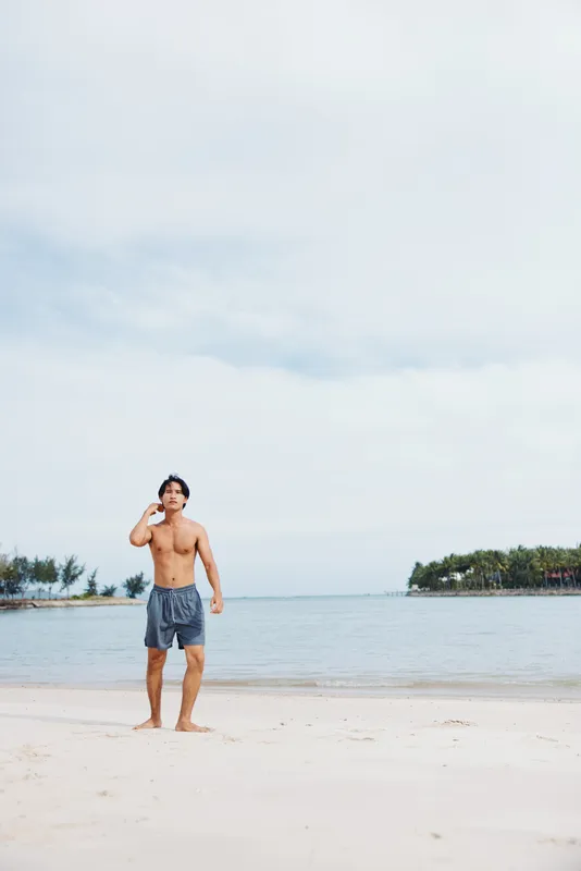Сильный азиатский спортсмен бежит по пляжу на закате, излучая мощь и свободу
