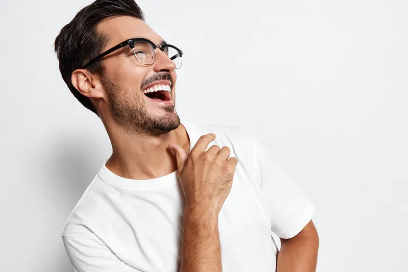 Full body laughing happy cheerful young caucasian man wear casual white t-shirt look away hand on shoulder isolated on plain solid light background studio portrait.